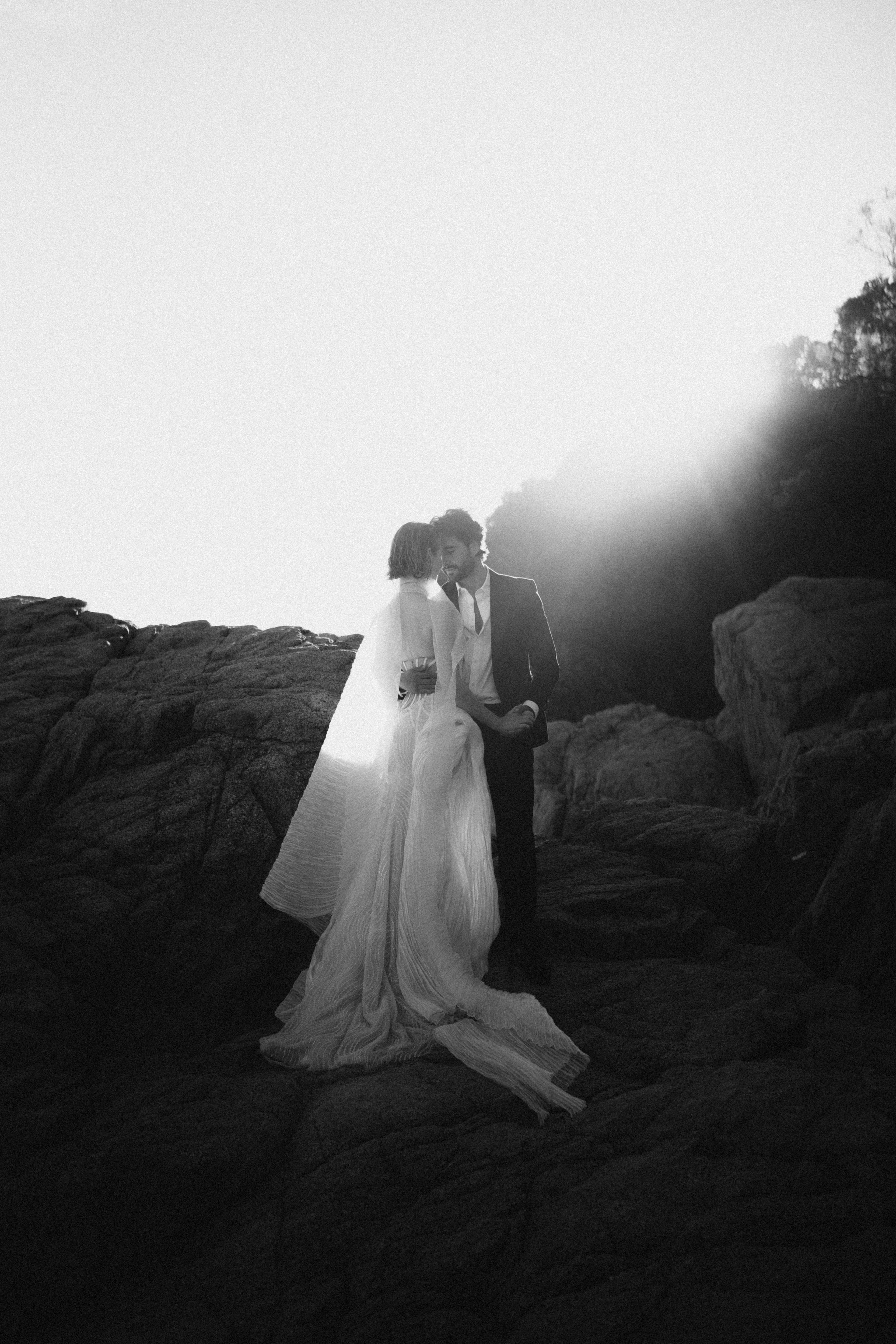 A black-and-white portrait among coastal rocks.