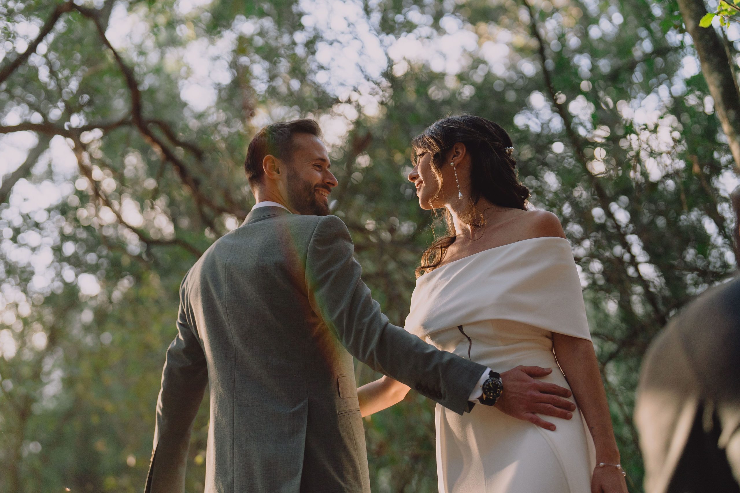 A couple turns towards each other beneath the trees.