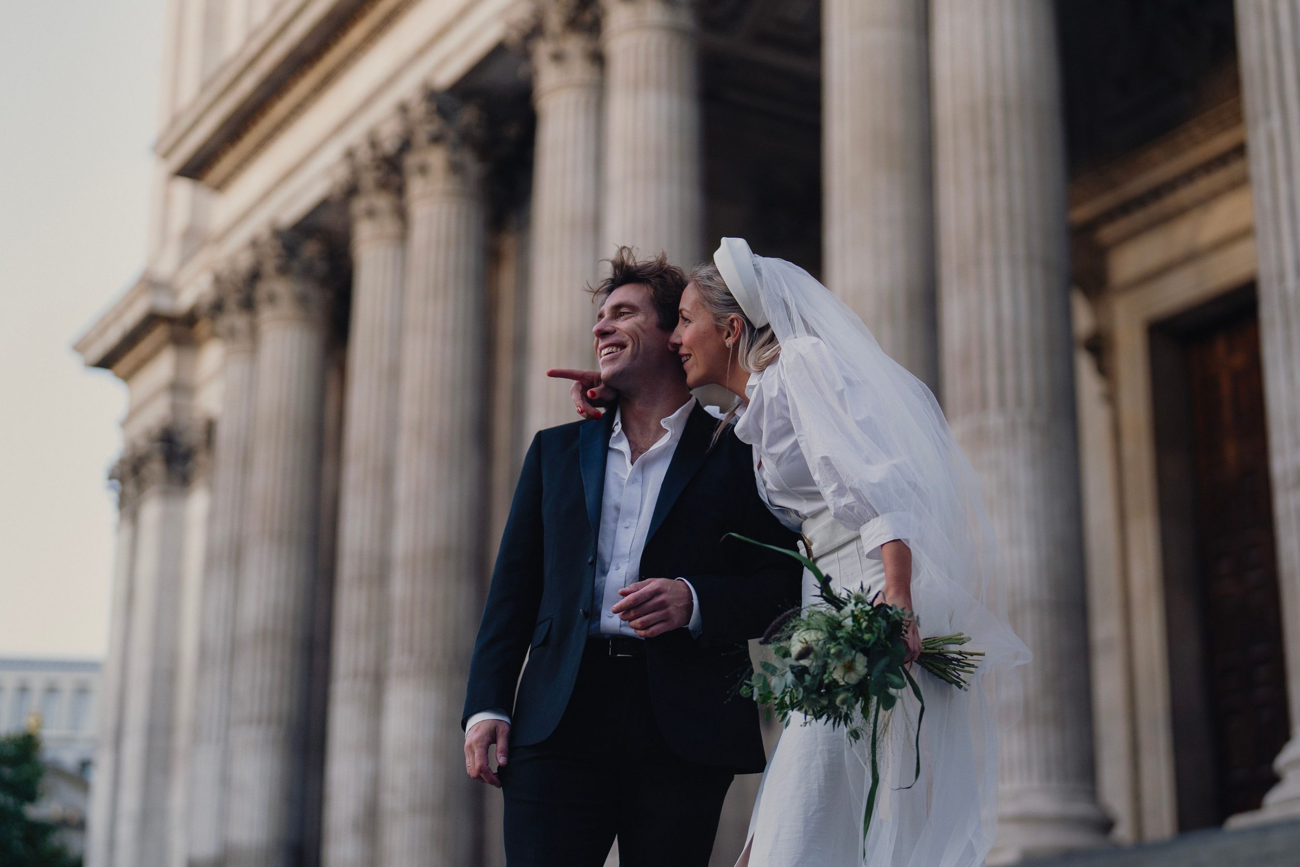 A couple walks beside the columns of a city building.