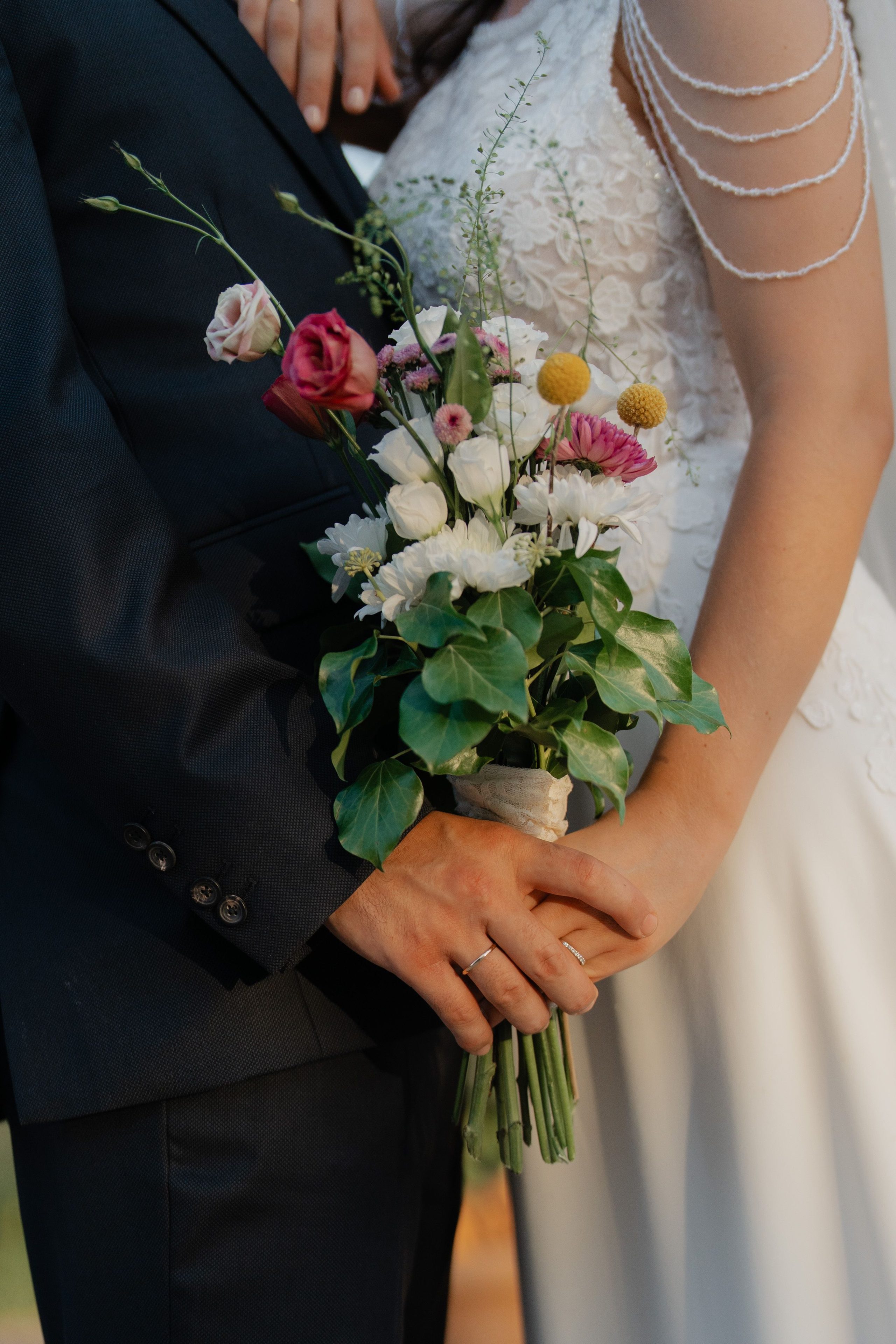 Hands together around the wedding bouquet.
