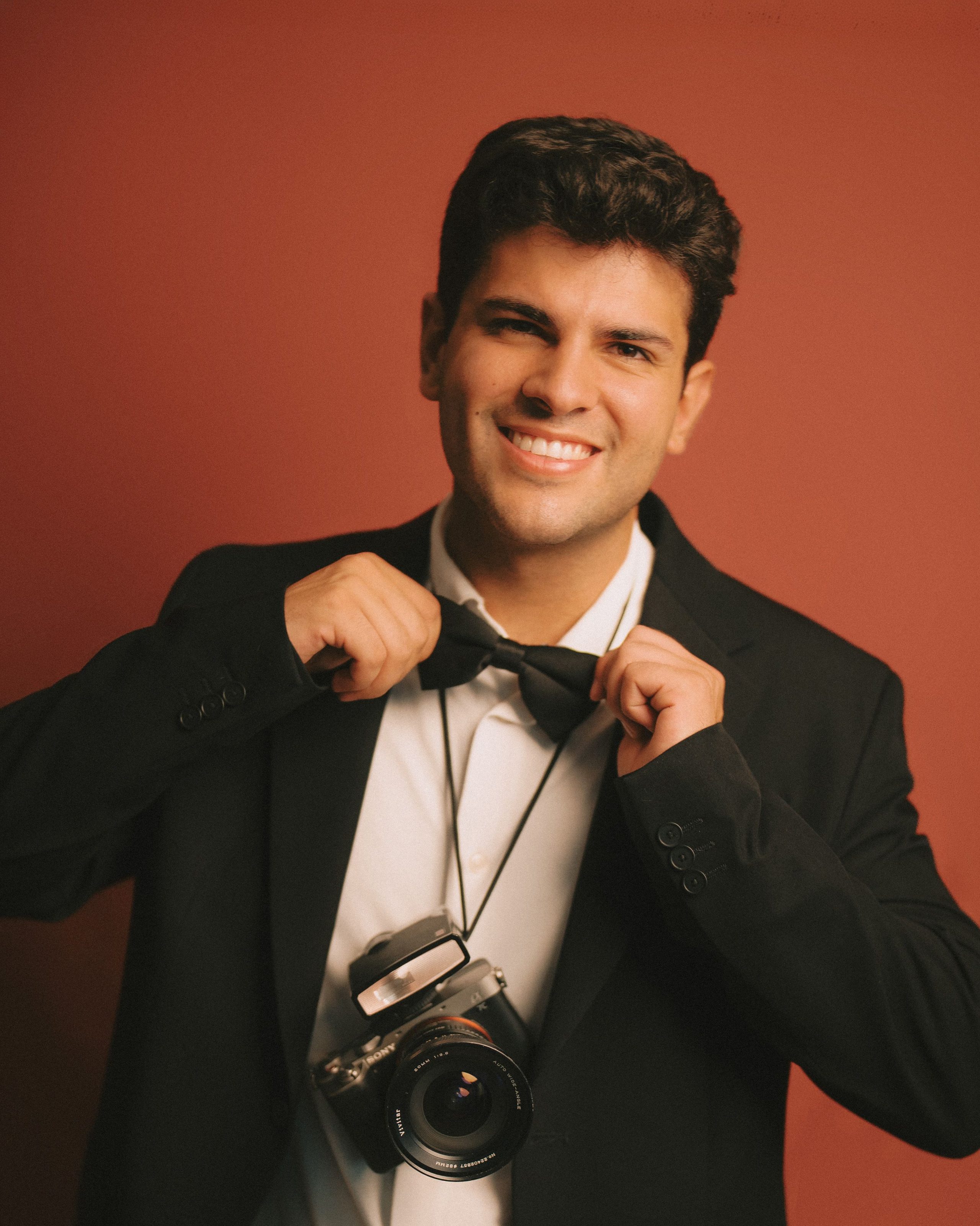 A photographer straightens his bow tie, camera at hand.