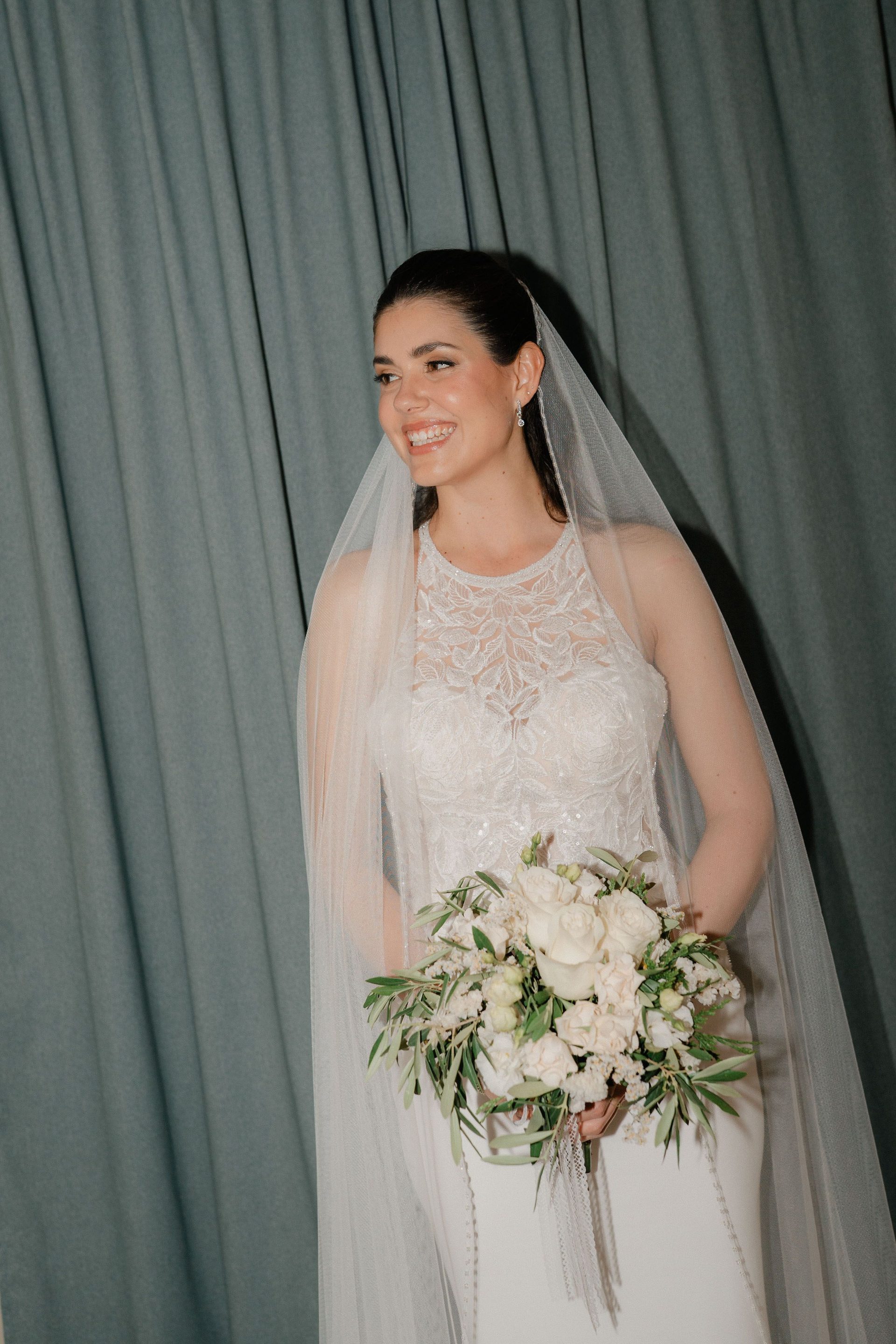 A bride and her bouquet against a curtain backdrop.