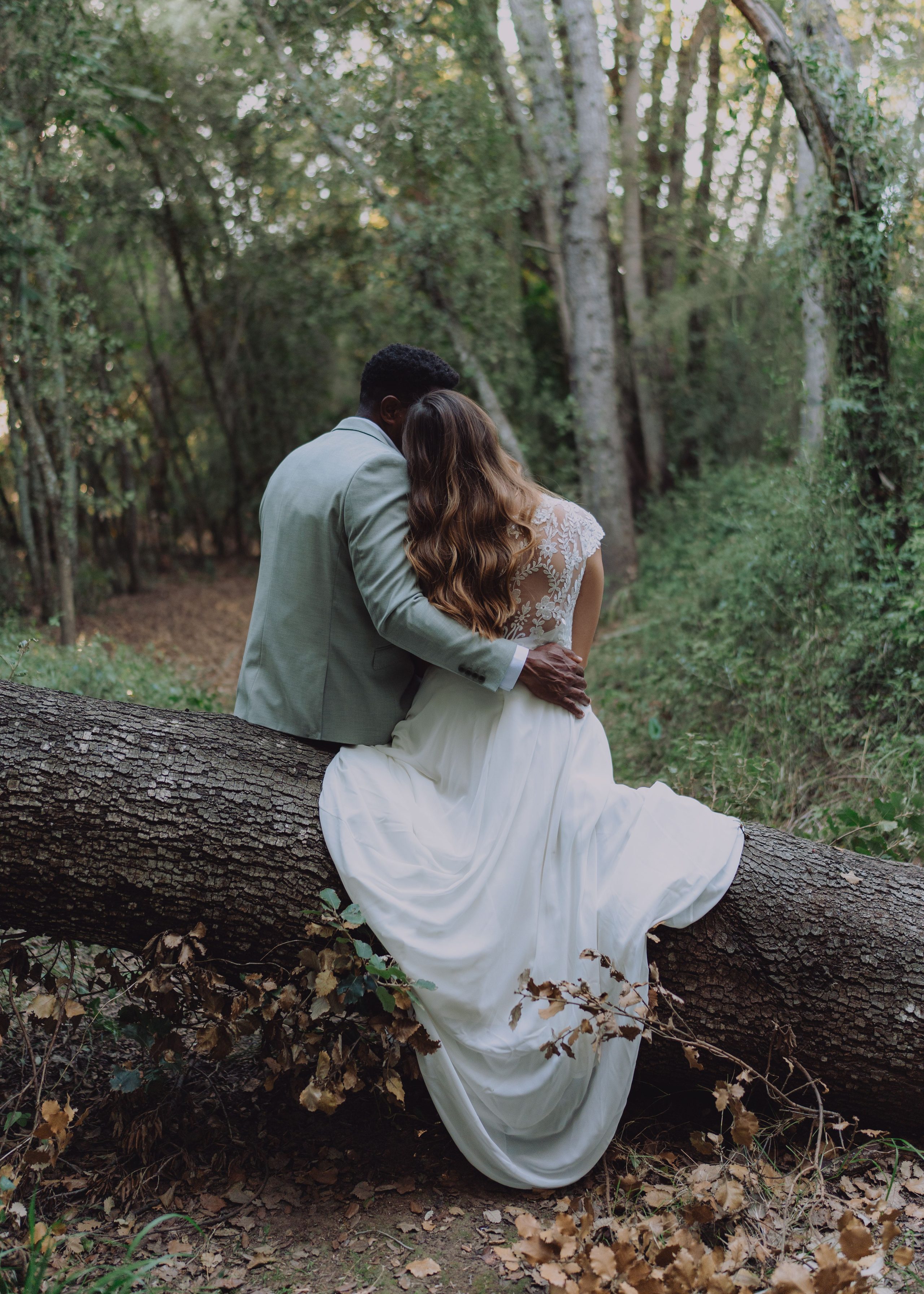 A couple sits close together on a fallen tree.